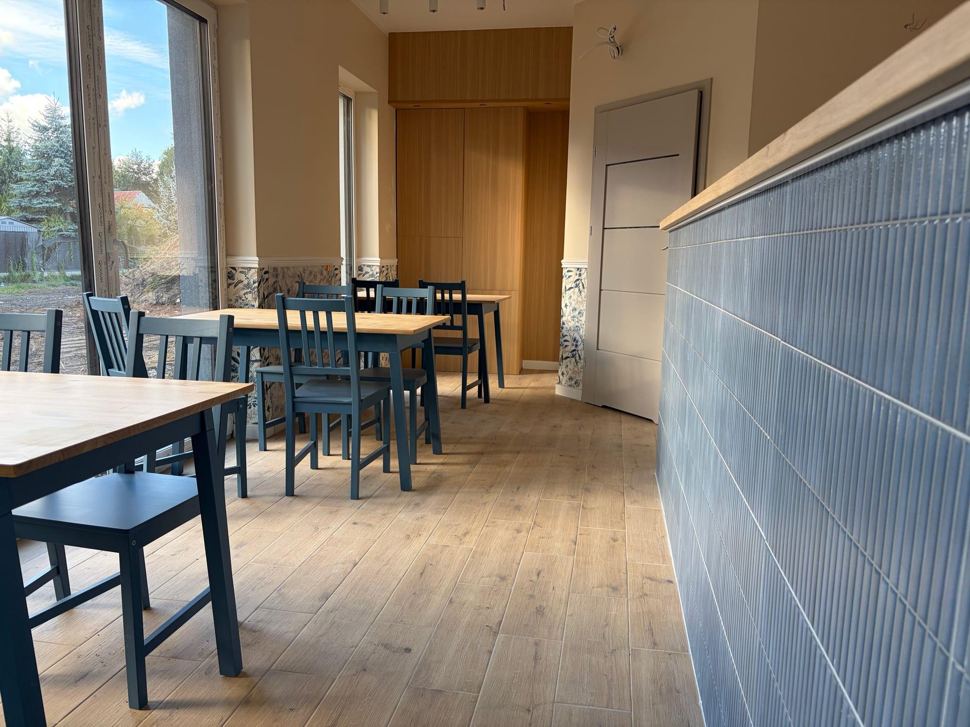 Sala bistro uPICHcone w Zieleniewie: drewniane stoły, granatowe krzesła i bar wyłożony niebieskimi płytkami, w świetle z dużych okien